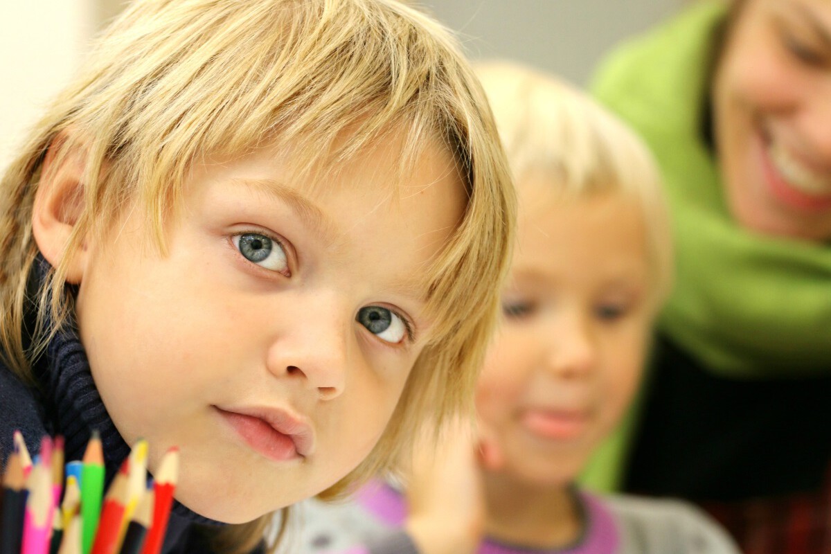 Junge in der Schule schaut in die Kamera, vor sich bunte Stifte