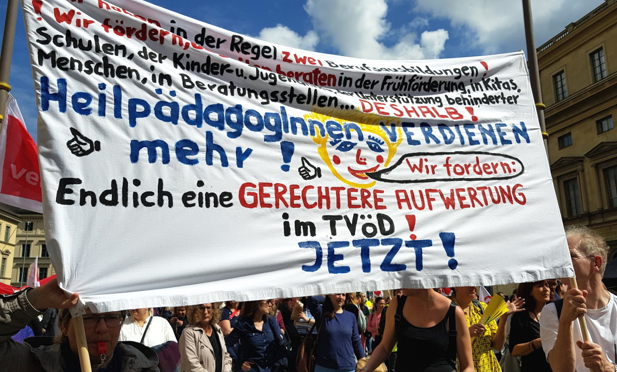 Abbildung zeigt Personen auf einem Streik, die ein Plakat hochhalten. Darauf stehen Forderungen für bessere Arbeitsbedingungen für HeilpädagogInnen