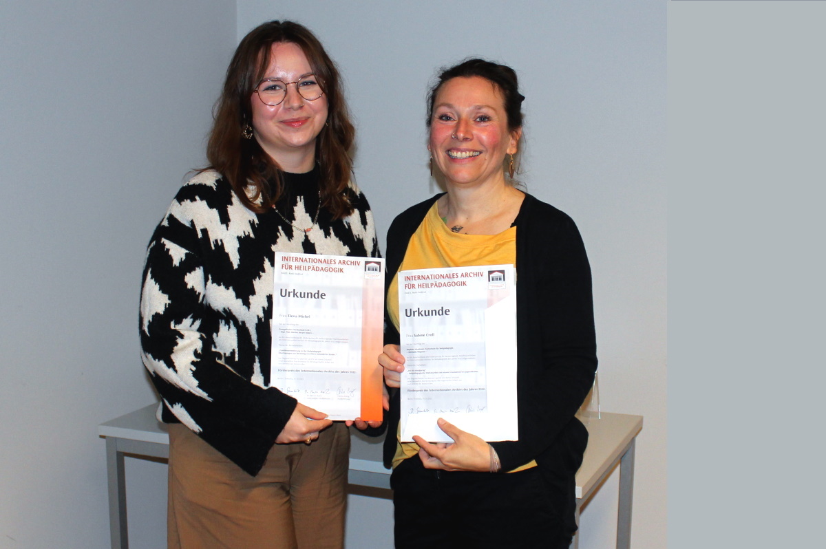 Das Bild zeigt die beiden Preisträgerinnen des Förderpreises vor einem weißen Hintergrund. Sie halten ihre Urkunden in den Händen.